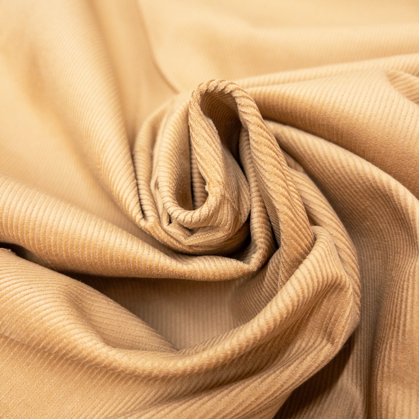 Light brown cotton corduroy garment fabric shown twisted in a spiral.
