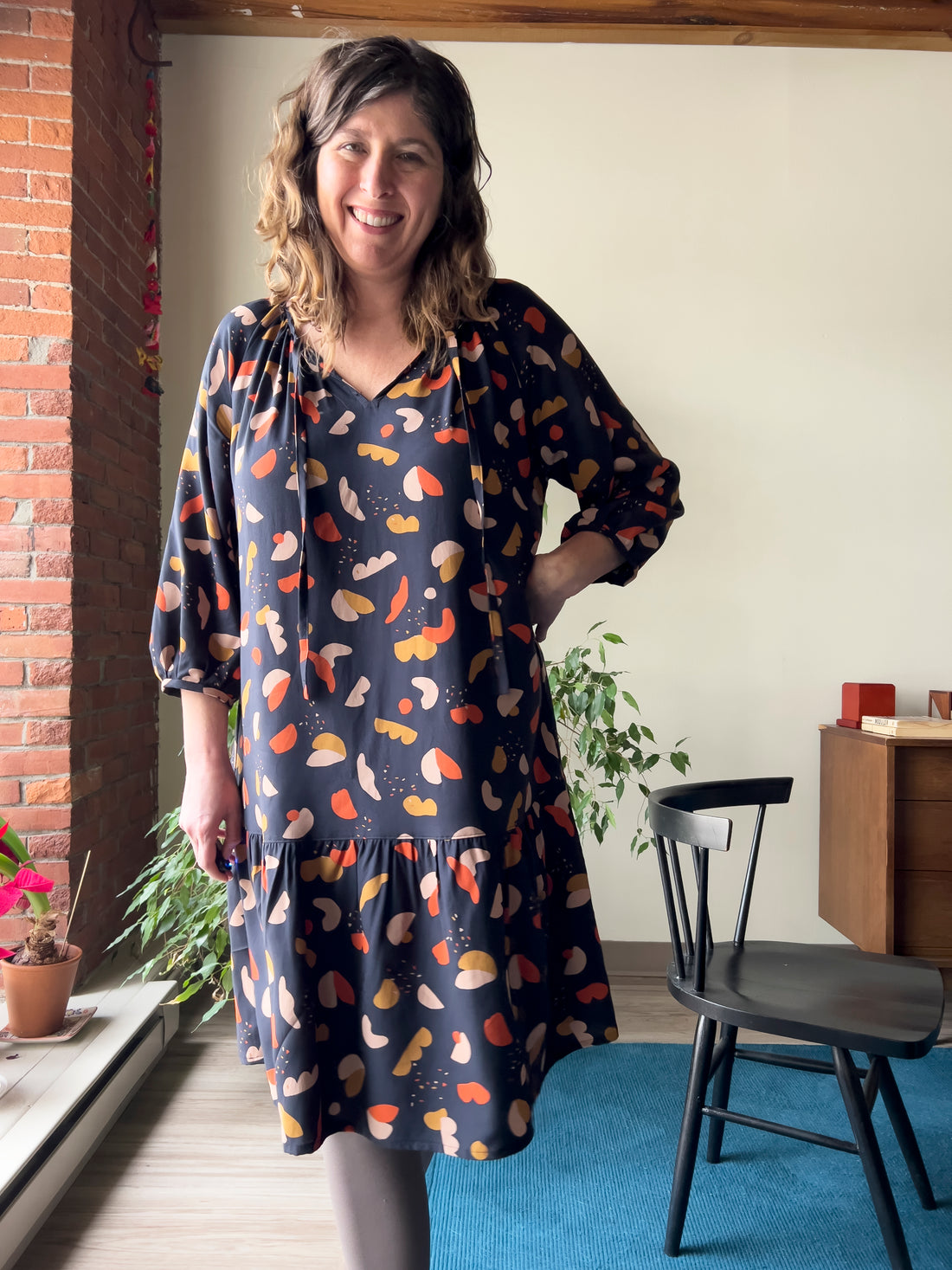 Image of a woman facing forward in The Roscoe Dress sewing pattern by True Bias.  The fabric is flowy with a off-black background with abstract shapes in saffron, mustard and chestnut colors.