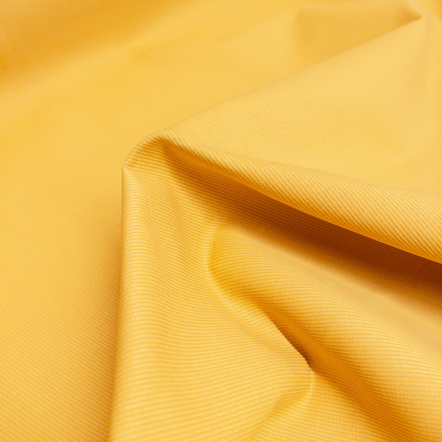 Cotton garment fabric in a pale yellow shown up close and folded to illustrate stiff fabric structure.