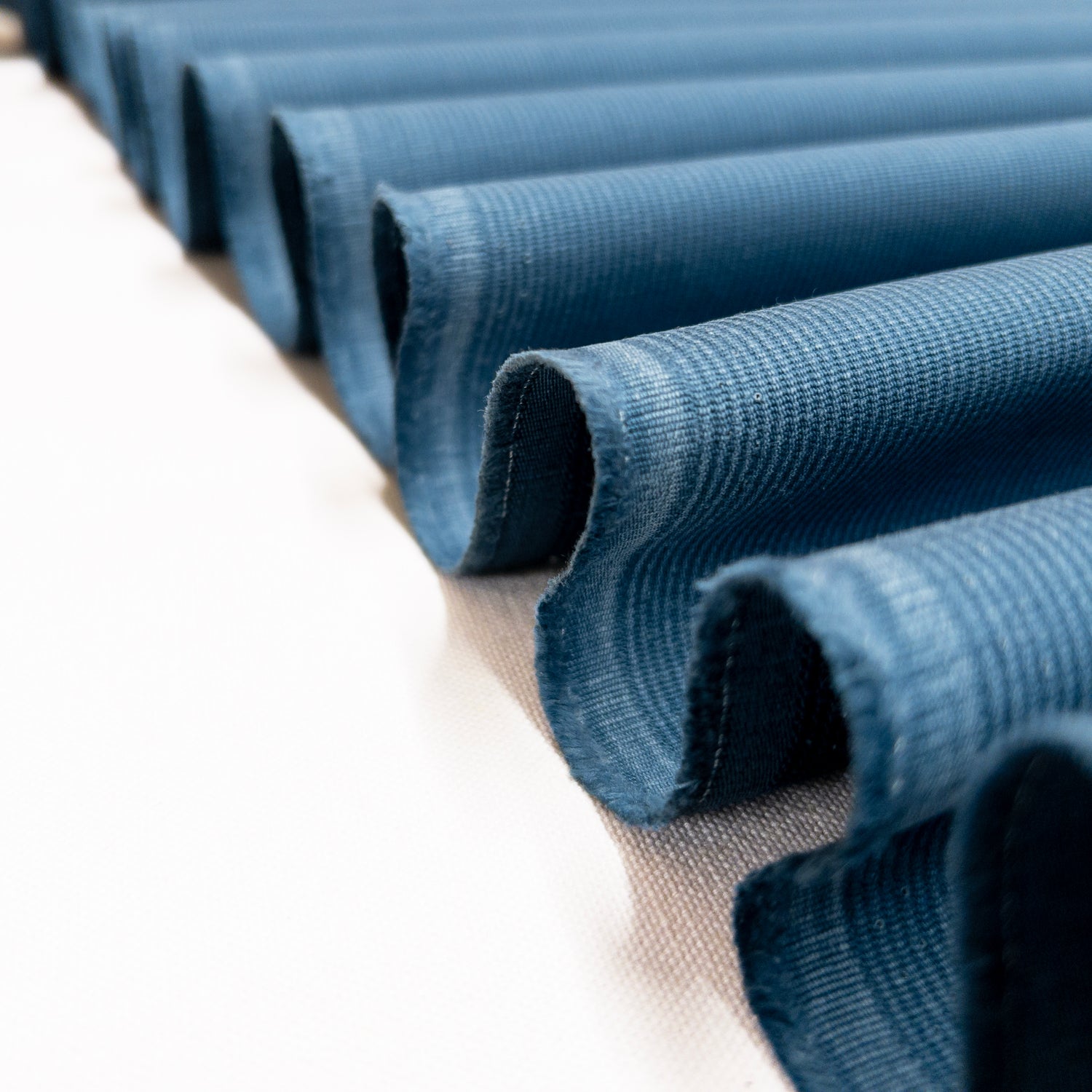 Blue garment fabric from 100% cotton with raised vertical ribs shown folded in a ribbon.