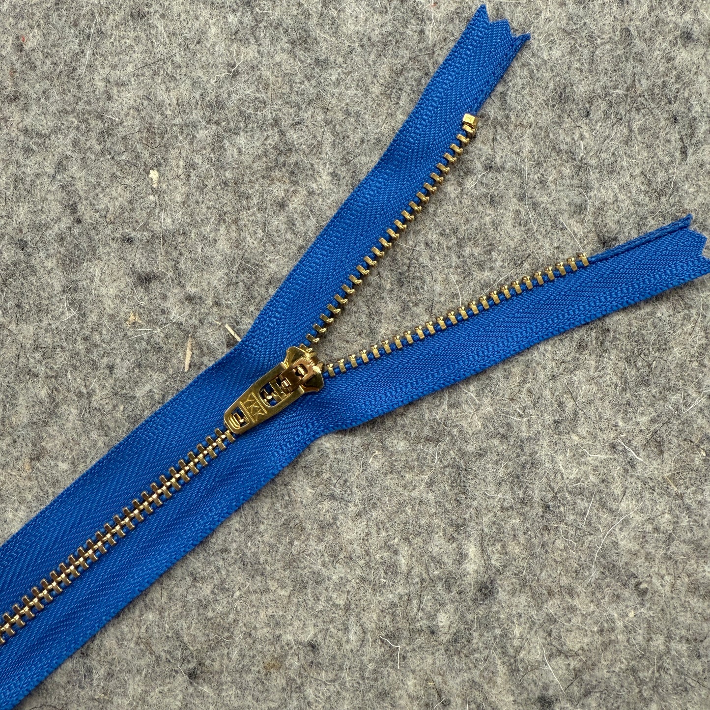 Blue zipper with gold metal teeth on a gray surface