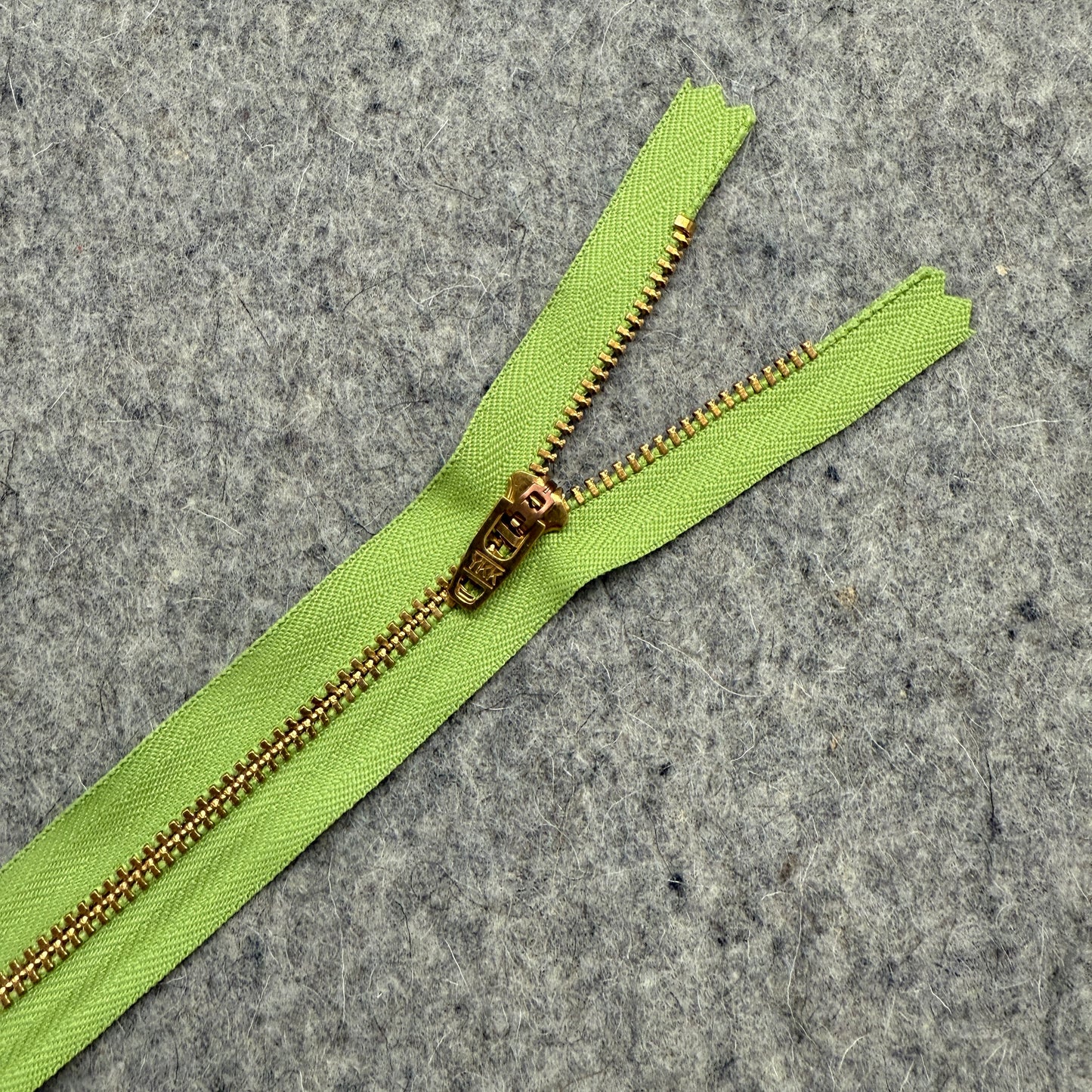 Green zipper with gold metal teeth on a gray textured background