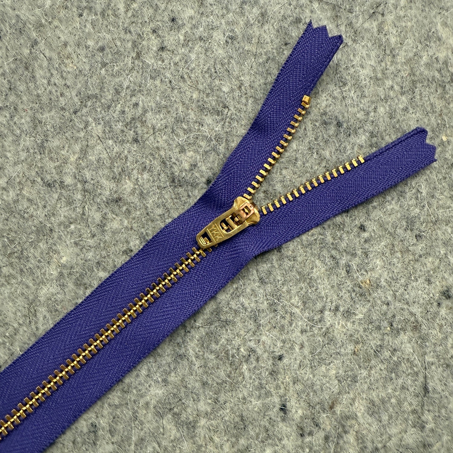 Purple zipper with gold teeth on a gray textured background