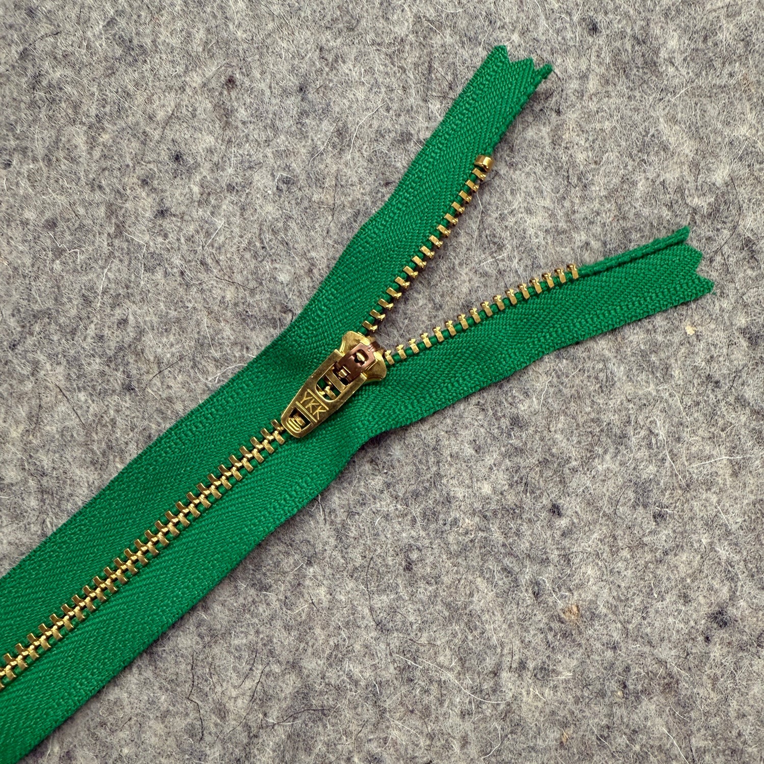 Green zipper with gold teeth on a gray surface