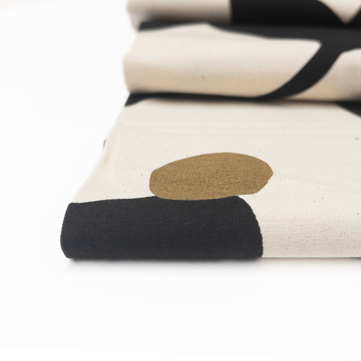 detail view of folded natural canvas fabric featuring a large print of black with bronze accents