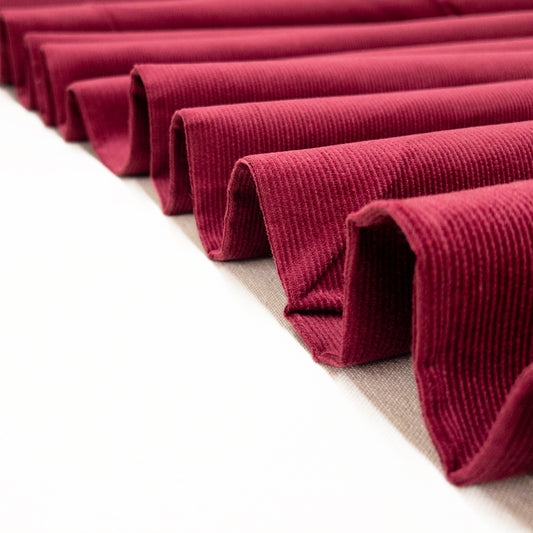 Cotton corduroy garment fabric in red Merlot shown folded like a ribbon.