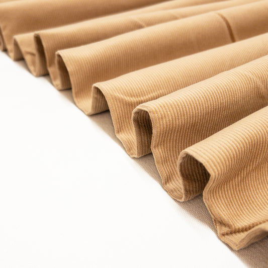 Cotton corduroy apparel fabric with a low cut pile shown folded like a ribbon.