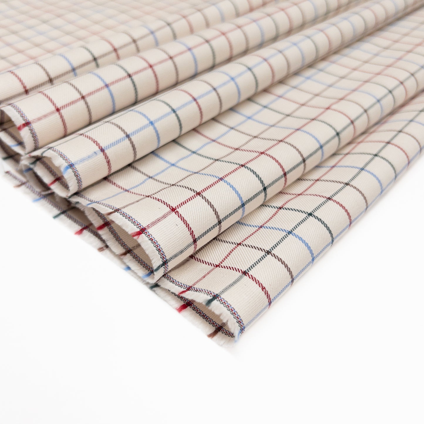 100% cotton shirting fabric in tattersall plaid features a multi color grid with a soft white base shown folded.