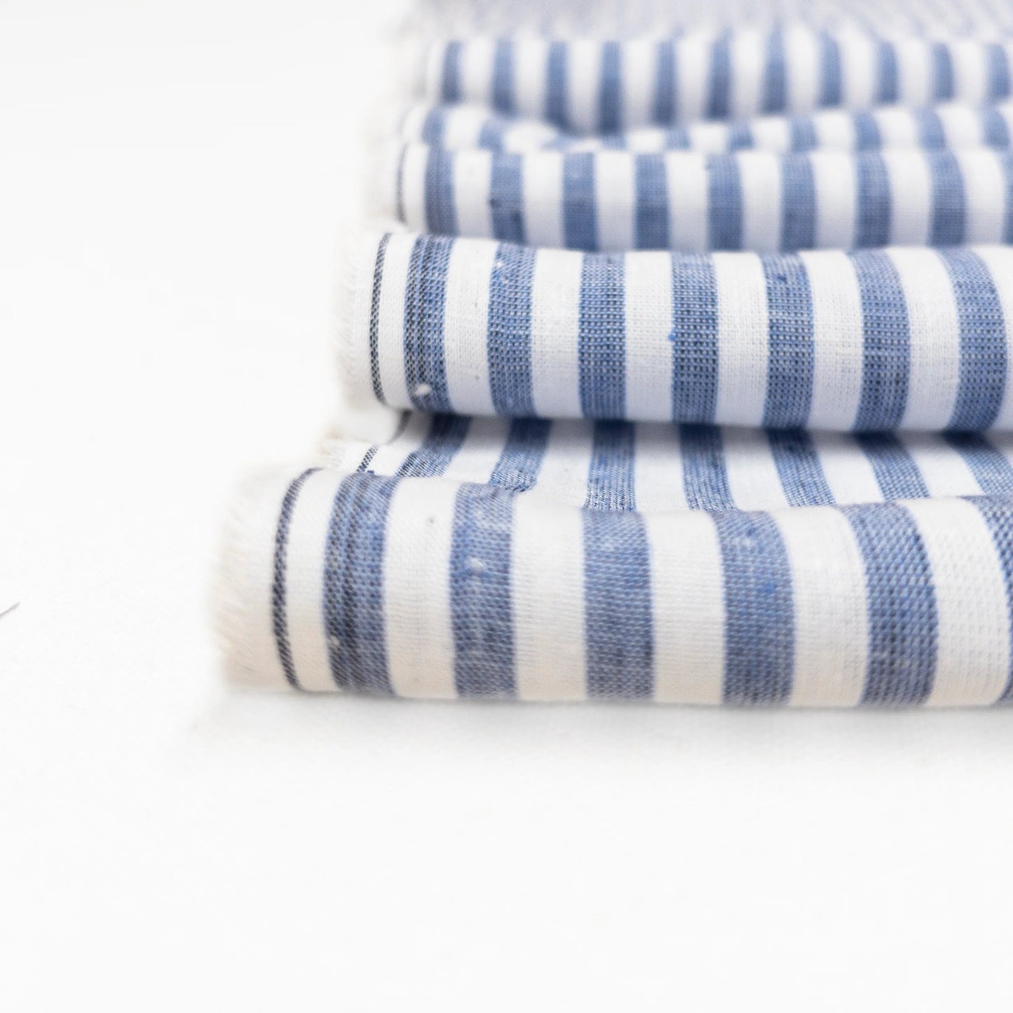 This lightweight cotton and linen garment fabric is shown in a detail view to see the weave and faded blue of the stripes.