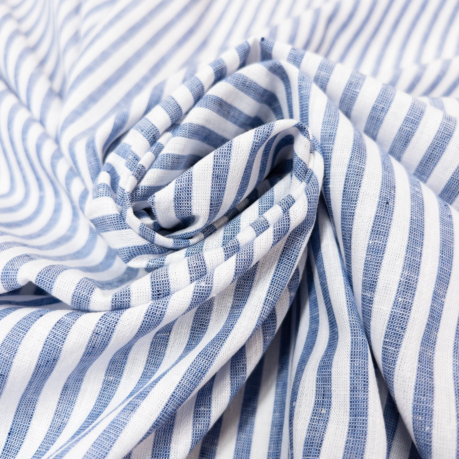 Fabir is spiraled illustrating the soft drape of this cotton linen garment fabric with blue and white stripes.