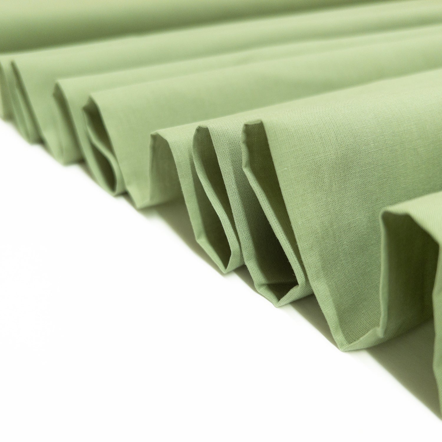 This garment fabric shown folded in a ribbon is a 100% cotton voile  in herb green