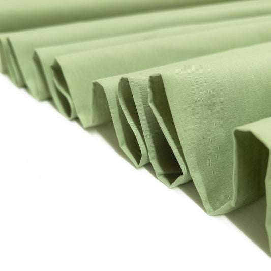 This garment fabric shown folded in a ribbon is a 100% cotton voile  in herb green