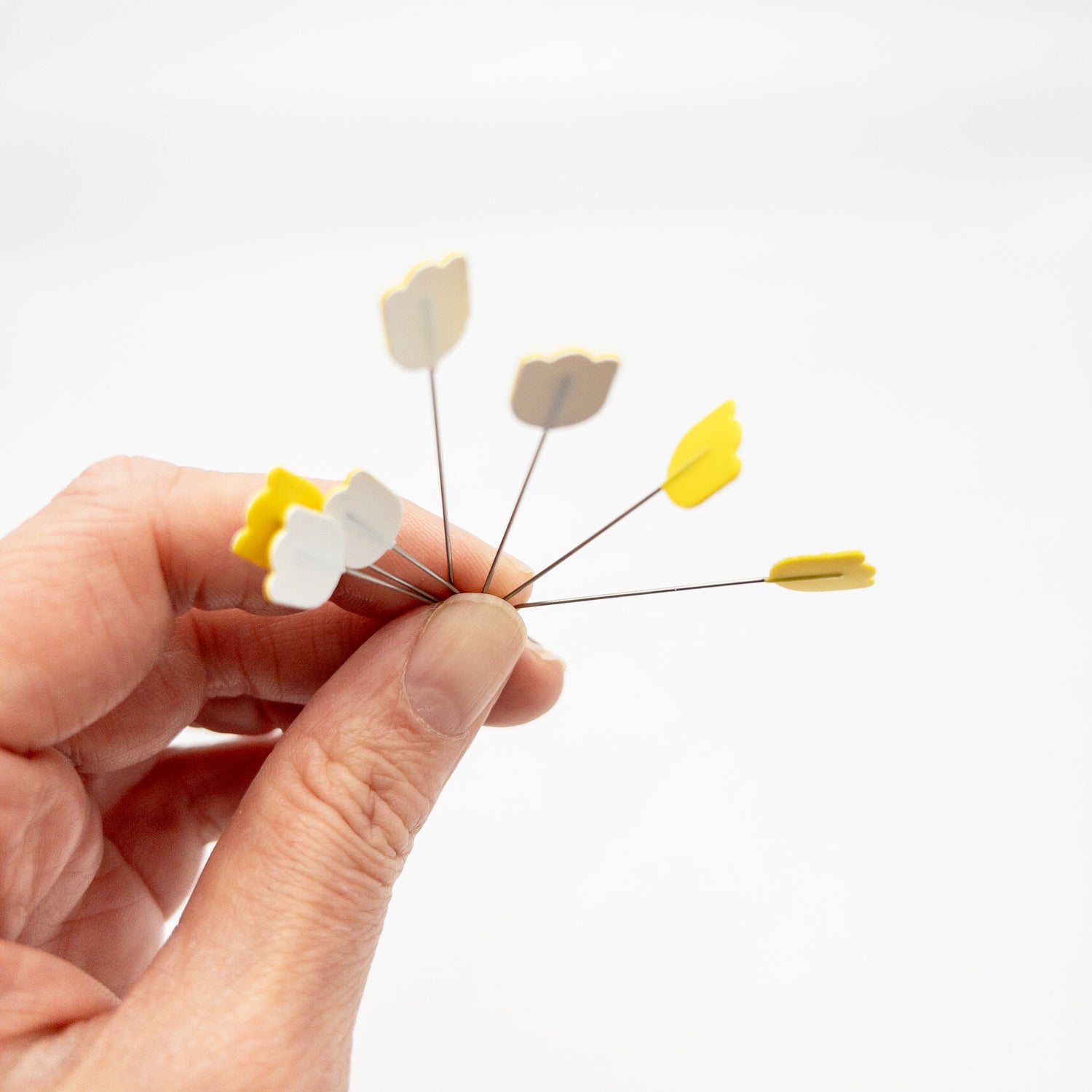 Hand holding several yellow and white tulip head pins for sewing.