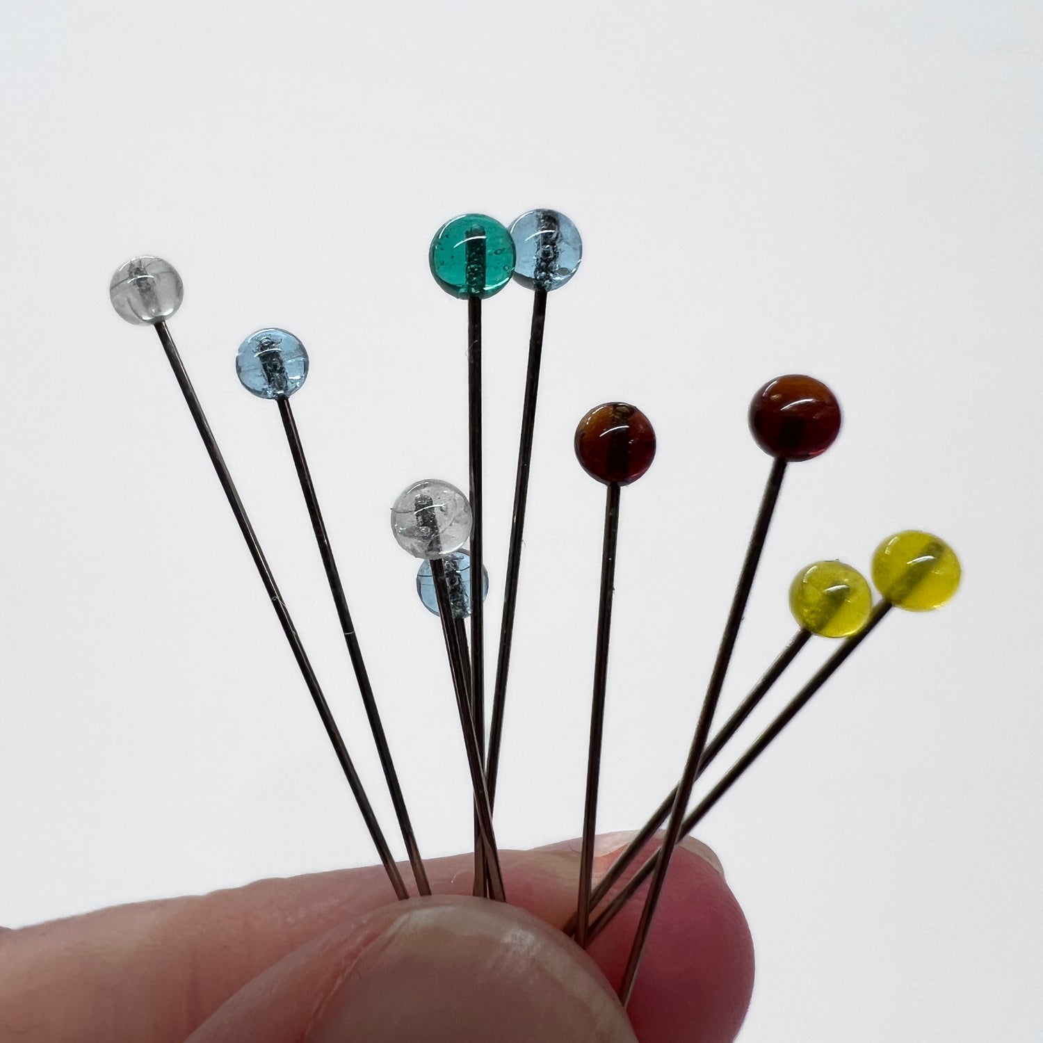 Sewing pins with translucent glass heads pinched in fingers seen from the side.