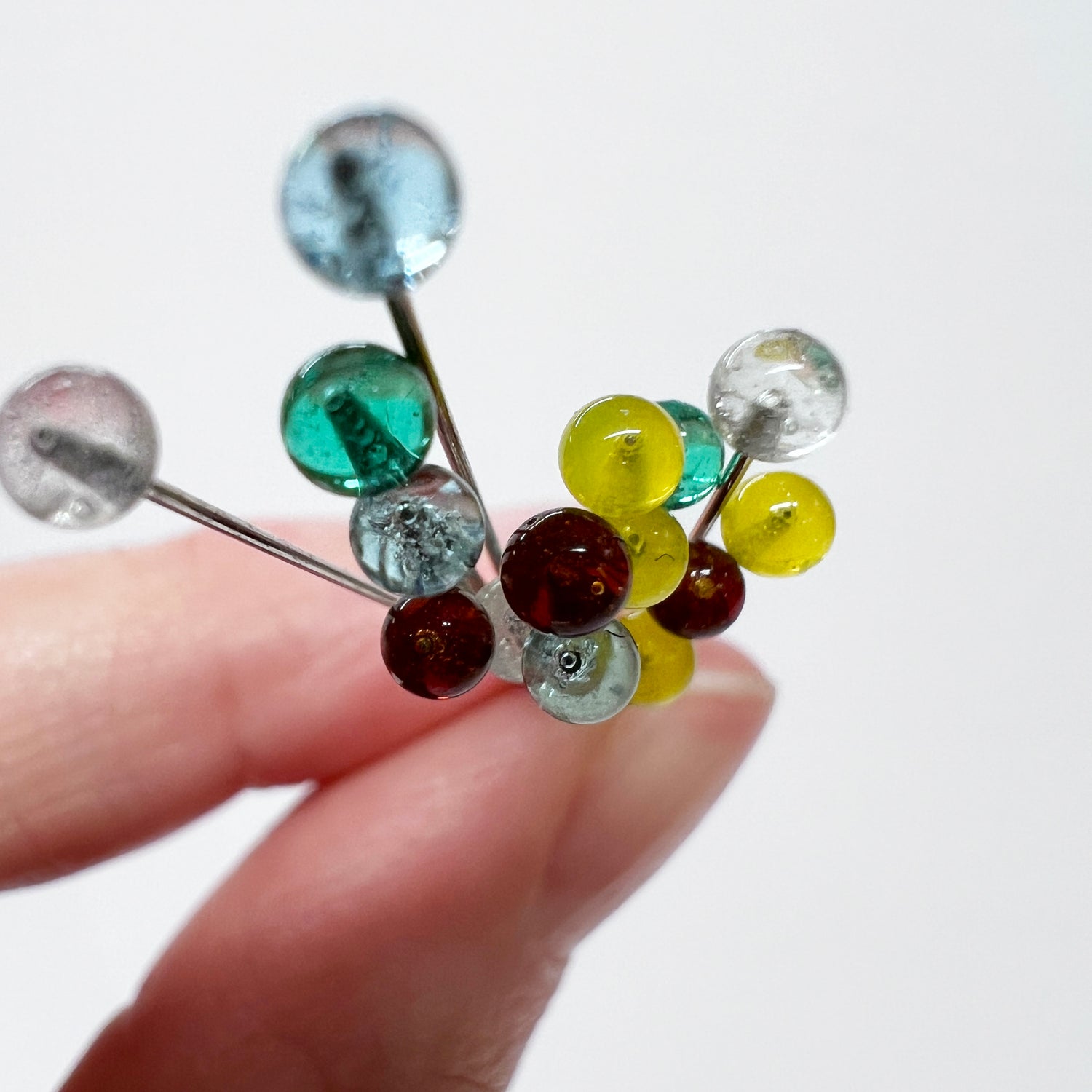 Fingers pinching several glass head sewing pins with a close up view of the multi color pin heads.