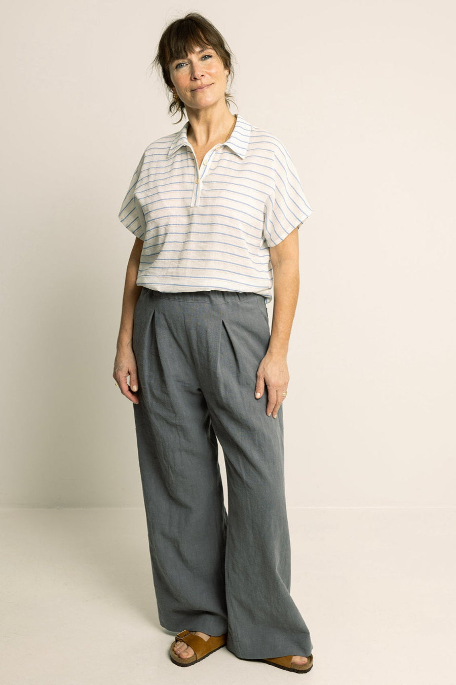 Woman wearing a striped shirt and gray wide-leg pants on a plain background