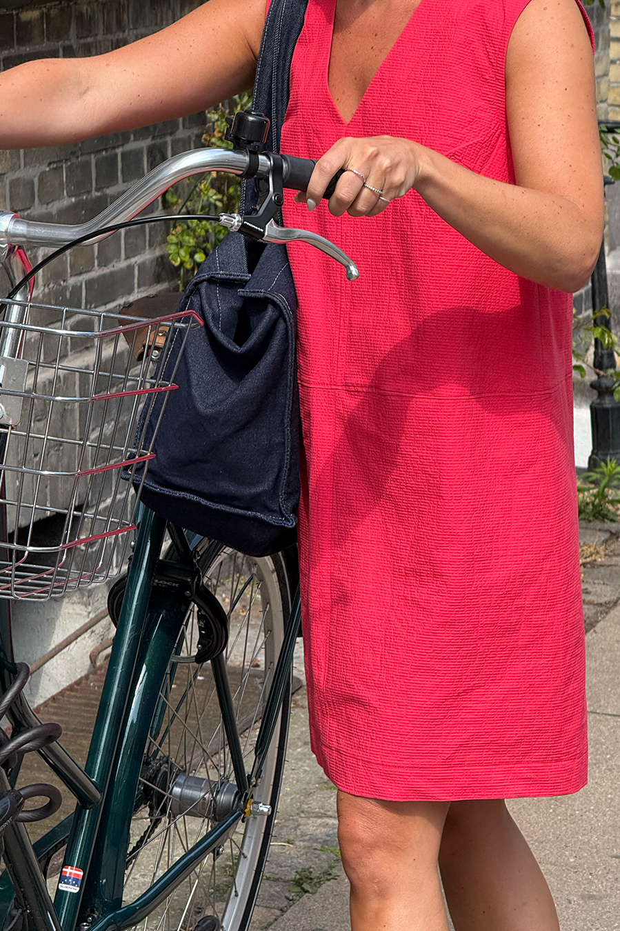 Woman in a red dress holding a navy bag next to a bicycle on a sidewalk.