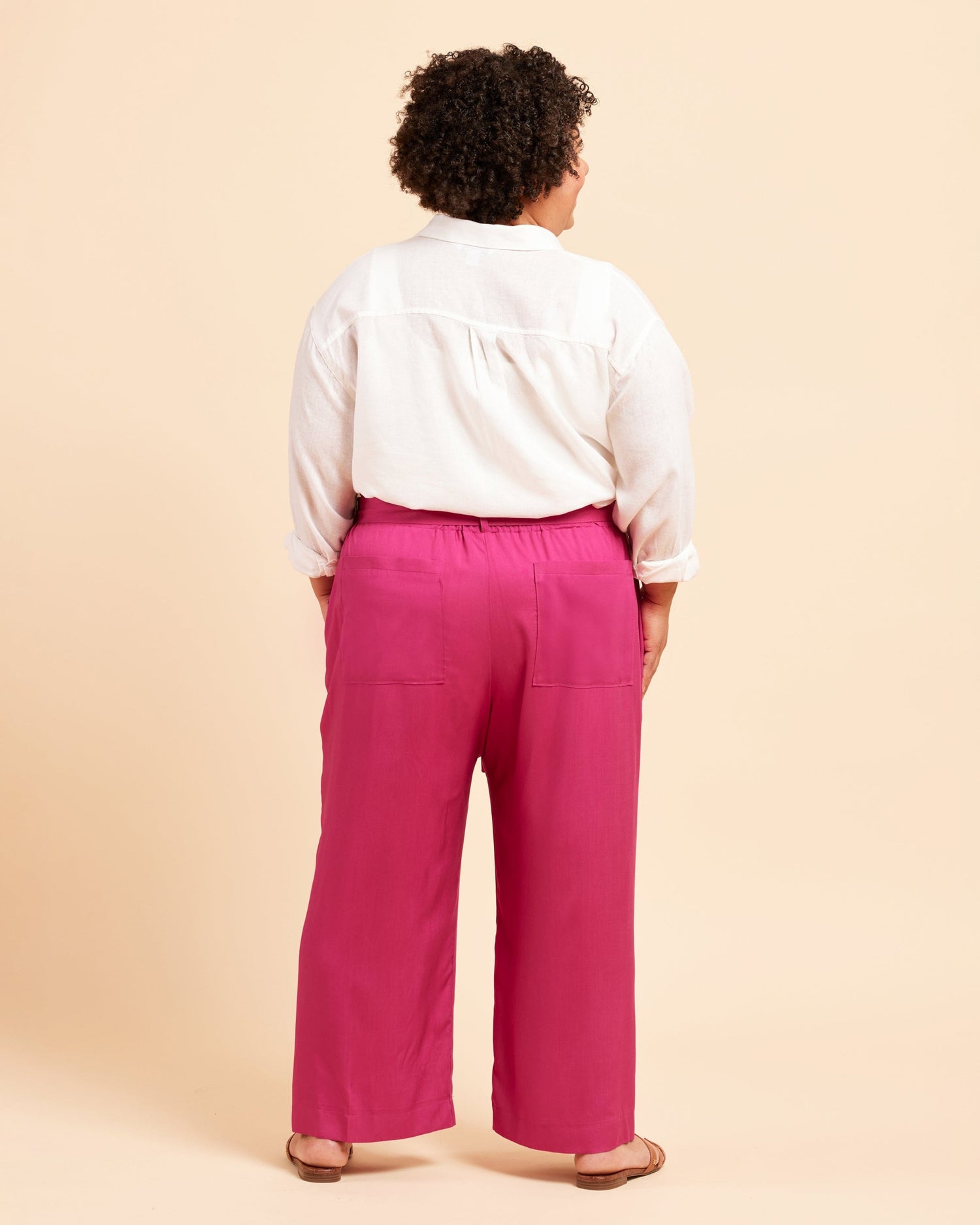 Person wearing a white shirt and pink pants on a beige background. These pants are the Everett Pants & Shorts sewing pattern from Cashmerette.